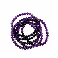 A coiled strand of polished purple gemstone beads, likely amethyst, arranged in a spiral on a solid white background.