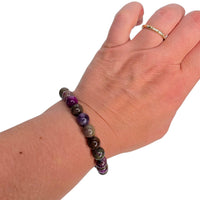 A multicolor beaded stretch bracelet made of polished stone beads with natural swirls, worn on a person's wrist. The person's hand and wrist are shown against a plain white background, with a gold ring visible on the index finger.