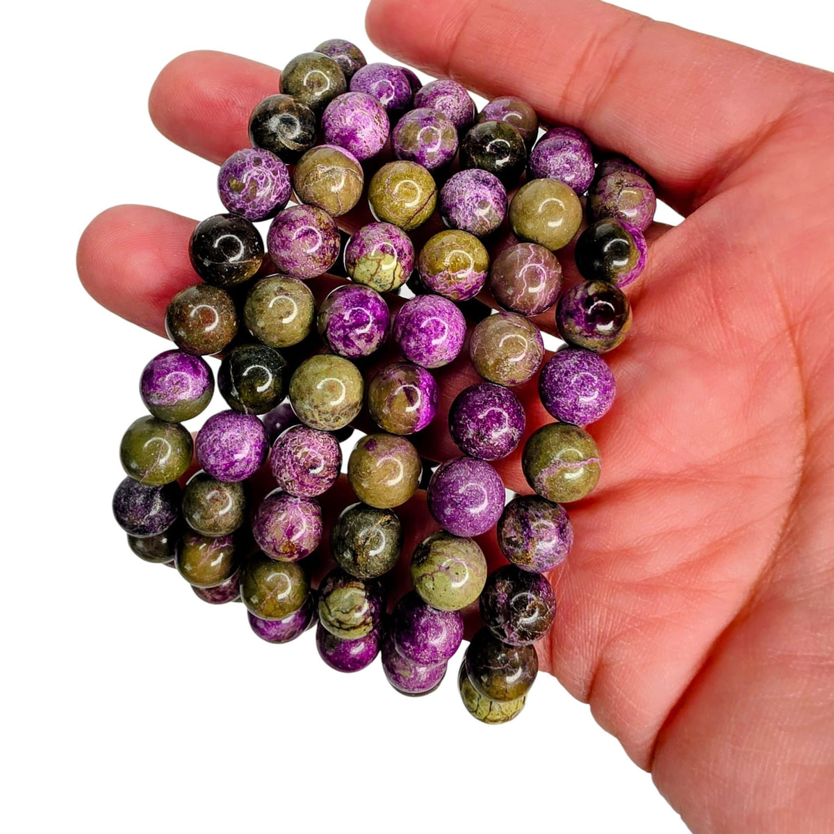 A hand holding a bundle of round, polished gemstone beads in purple, olive green, and black with natural marbled patterns, set against a plain white background.