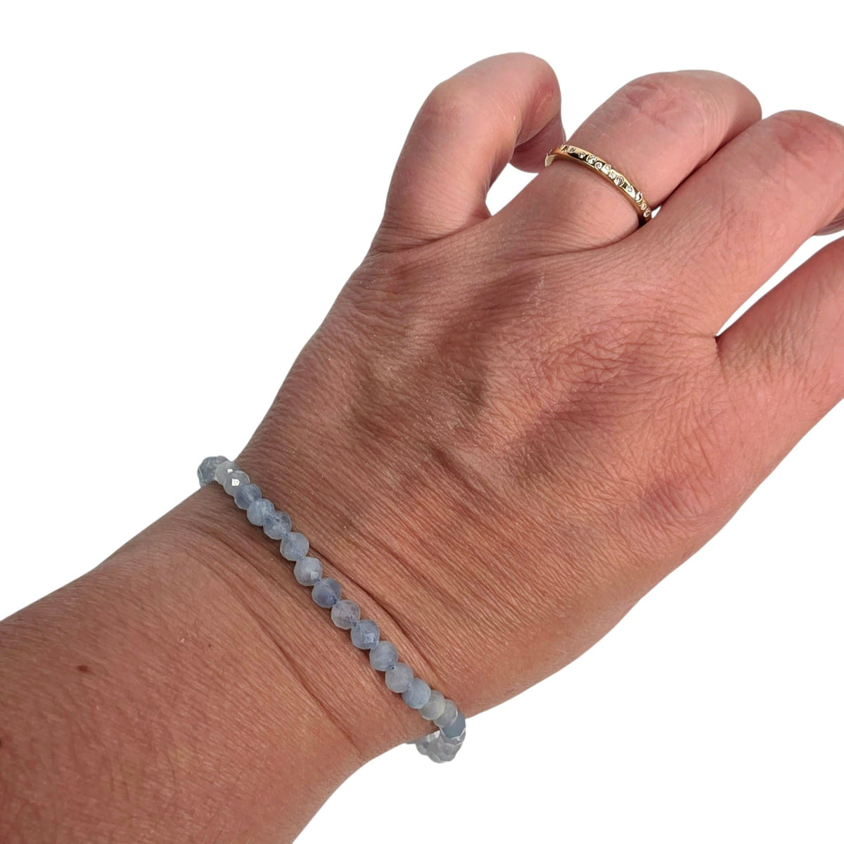 A light blue beaded bracelet worn on a person's wrist, with a gold ring on one of the fingers, shown against a plain white background.