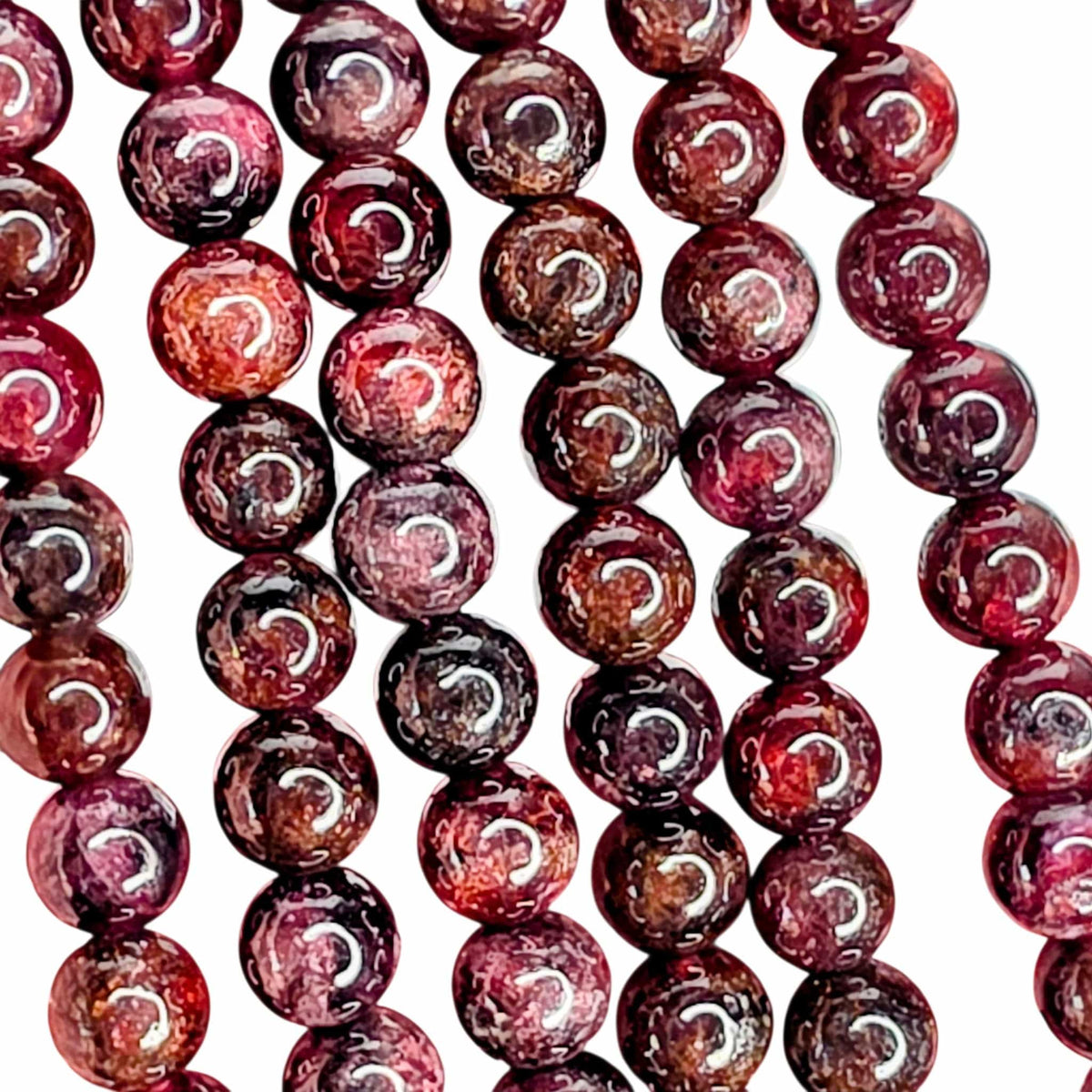 Close-up of multiple strands garnet beads, with glossy highlights reflecting off the curved surfaces, set against a plain white background.