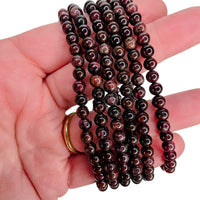 Three strands of polished garnet beads draped over a person's hand, with a gold ring visible on the wrist against a plain white background.