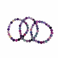 Three beaded stretch bracelets made of polished round gemstone beads in purple, pink, blue, green, and black, arranged overlapping on a plain white background.