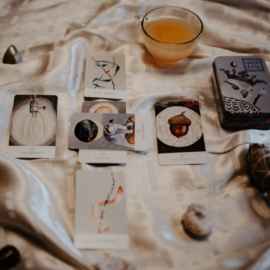 Tarot deck box with several card faces arranged on cloth and small candle cup